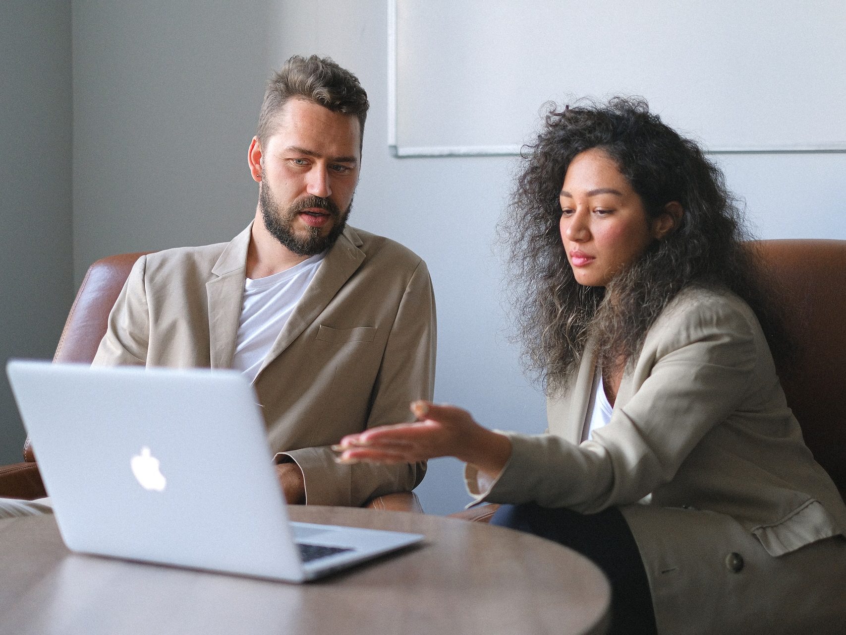 Serious colleagues in stylish outfits sitting at table and using laptop while discussing new project in office